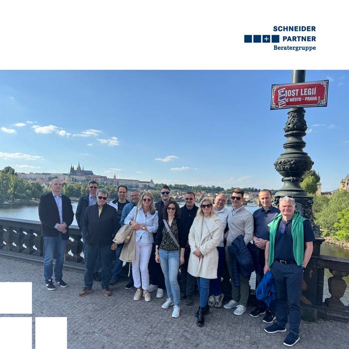 Mehrere Personen stehen beisammen auf einer alten Brücke vor dem Hintergrund der Prager Altstadt.